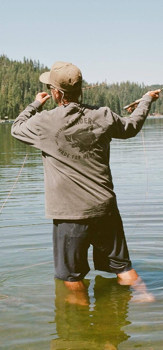 A man fly-fishing in a lake wearing a grey Seager Co. long sleeve tee and a snapback cap
