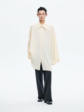 A man wearing a cream oversized wide-sleeve Sean Suen shirt and charcoal flared trousers