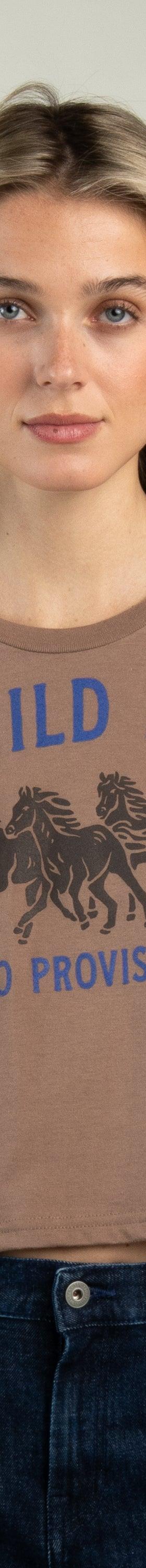A woman wearing a brown Sendero Provisions Co. Wild Horses cropped tee with dark denim jeans