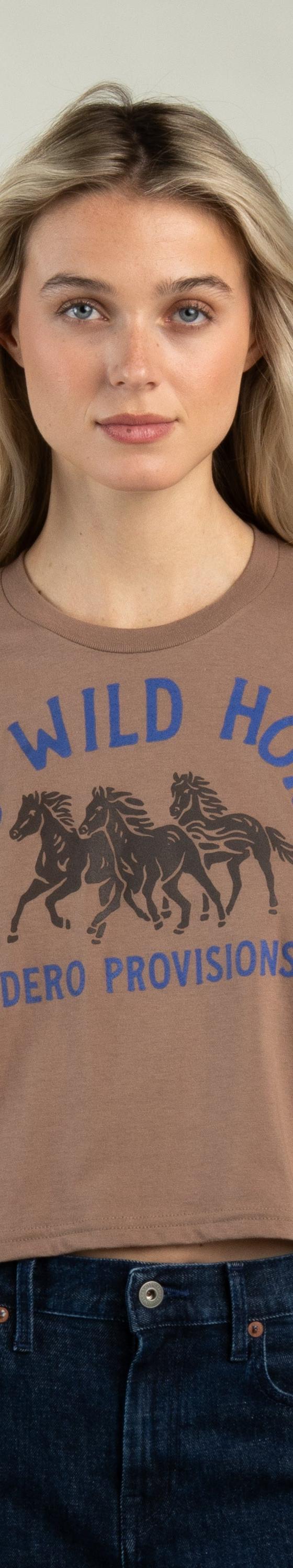 A woman wearing a brown Sendero Provisions Co. Wild Horses cropped tee with dark denim jeans
