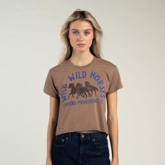 A woman wearing a brown Sendero Provisions Co. Wild Horses cropped tee with dark denim jeans