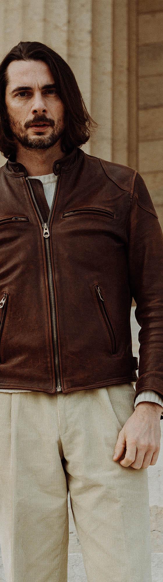 A man wearing a brown Shangri-La Heritage horsehide café racer jacket with cream trousers