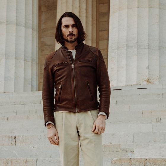 A man wearing a brown Shangri-La Heritage horsehide café racer jacket with cream trousers