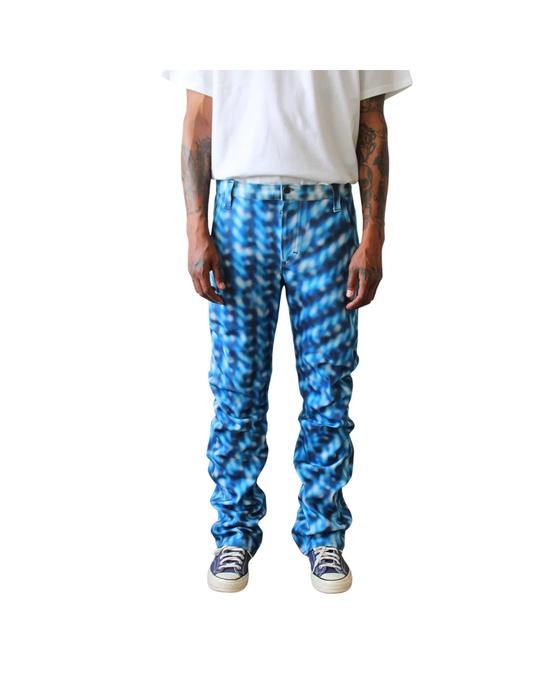 A man wearing blue Optical Wave print stacked Sheila Rashid jeans with a white T-shirt and navy sneakers