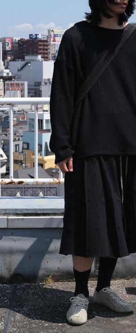 A man wearing a black SHINYAKOZUKA knit sweater and pleated skirt on a Tokyo rooftop