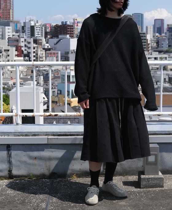 A man wearing a black SHINYAKOZUKA knit sweater and pleated skirt on a Tokyo rooftop
