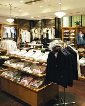 Interior of SHIPS Ginza (men): wood tables of folded shirts, racks of tailoring, no people
