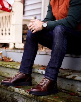 A man wearing brown Shoe The Bear leather lace-up boots with dark jeans, seated on porch steps
