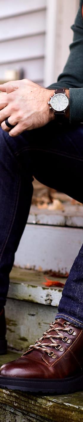 A man wearing brown Shoe The Bear leather lace-up boots with dark jeans, seated on porch steps