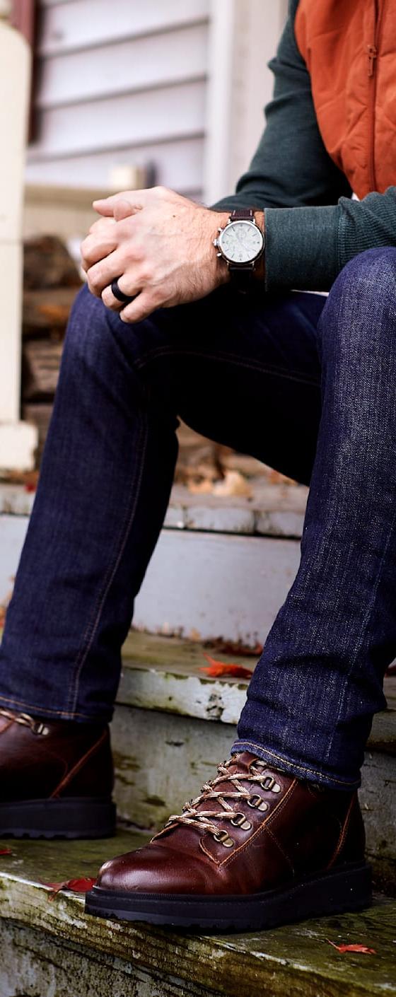 A man wearing brown Shoe The Bear leather lace-up boots with dark jeans, seated on porch steps