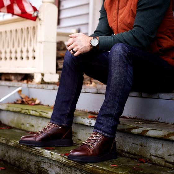 A man wearing brown Shoe The Bear leather lace-up boots with dark jeans, seated on porch steps
