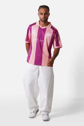 A man wearing a pink and purple striped Sixth June football jersey with white wide-leg trousers