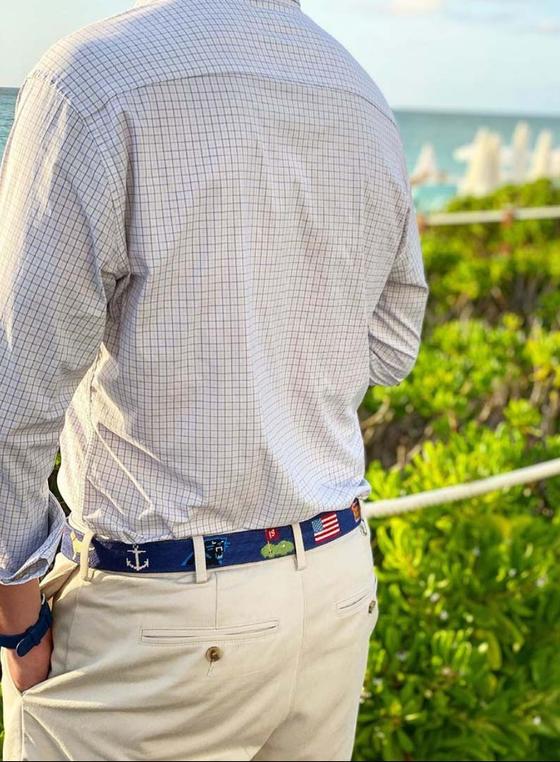 A man wearing a navy needlepoint Smathers & Branson belt with khaki trousers and a checked shirt by the sea