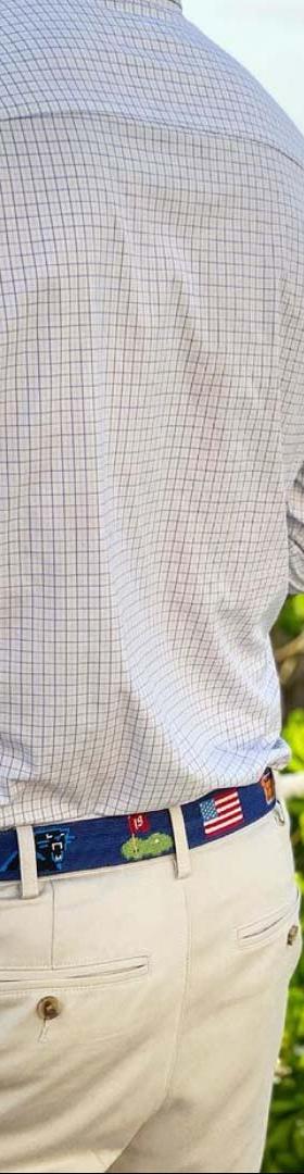 A man wearing a navy needlepoint Smathers & Branson belt with khaki trousers and a checked shirt by the sea