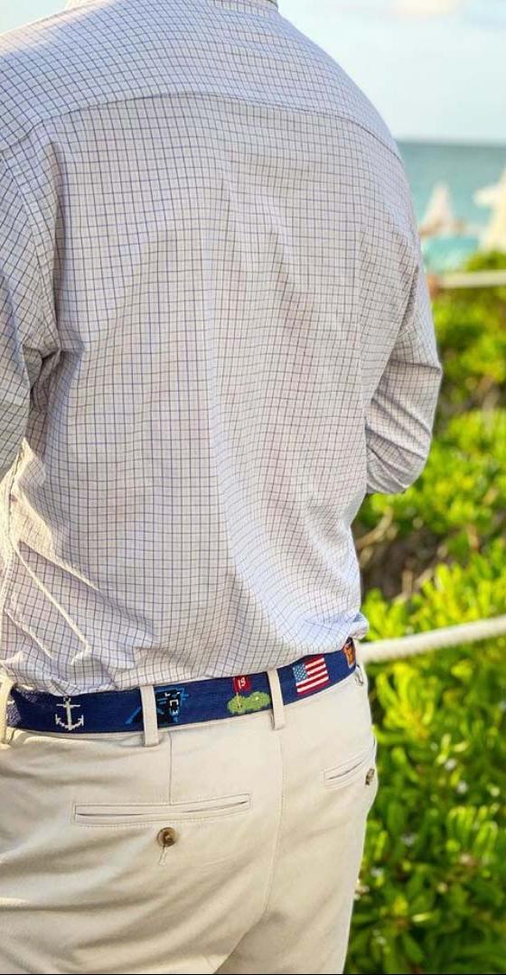 A man wearing a navy needlepoint Smathers & Branson belt with khaki trousers and a checked shirt by the sea