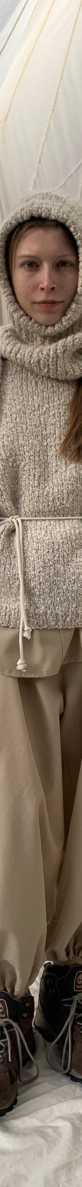 A woman wearing a cream SONO wool knit sweater and hood with beige trousers
