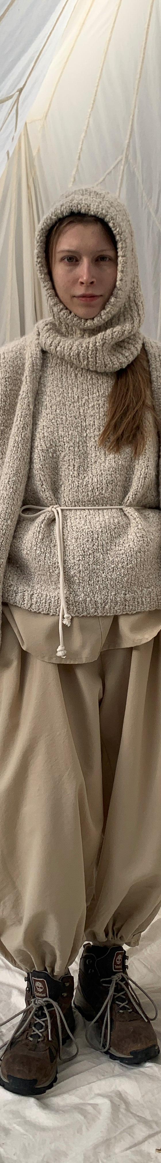 A woman wearing a cream SONO wool knit sweater and hood with beige trousers