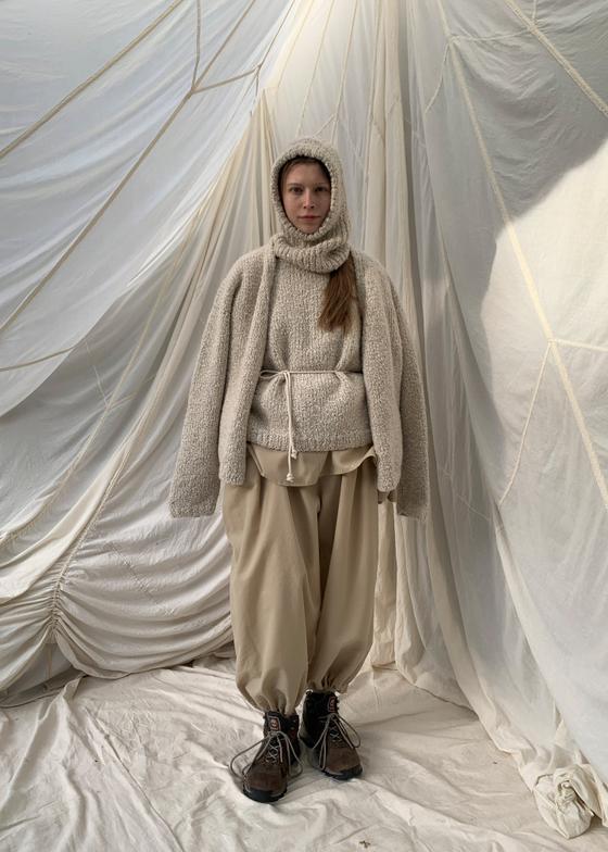 A woman wearing a cream SONO wool knit sweater and hood with beige trousers