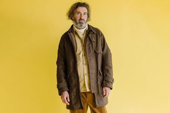 A man wearing a brown Soundman field jacket over a mustard shirt and corduroy trousers
