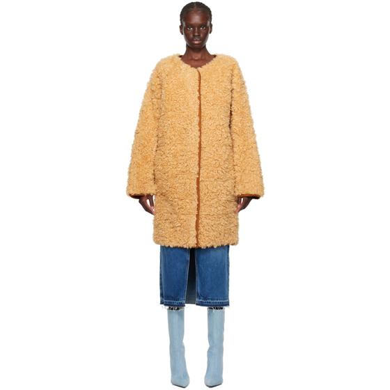 A woman wearing a beige faux fur Stand Studio coat with jeans and blue boots