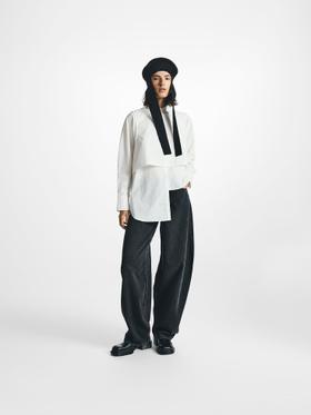 A woman wearing a white asymmetric STEL shirt with wide black denim trousers and a knit hood