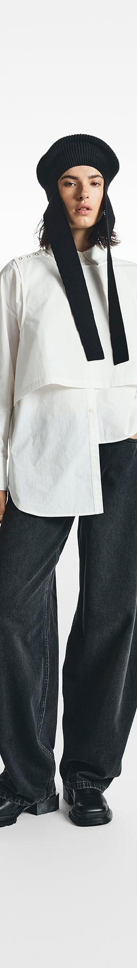 A woman wearing a white asymmetric STEL shirt with wide black denim trousers and a knit hood