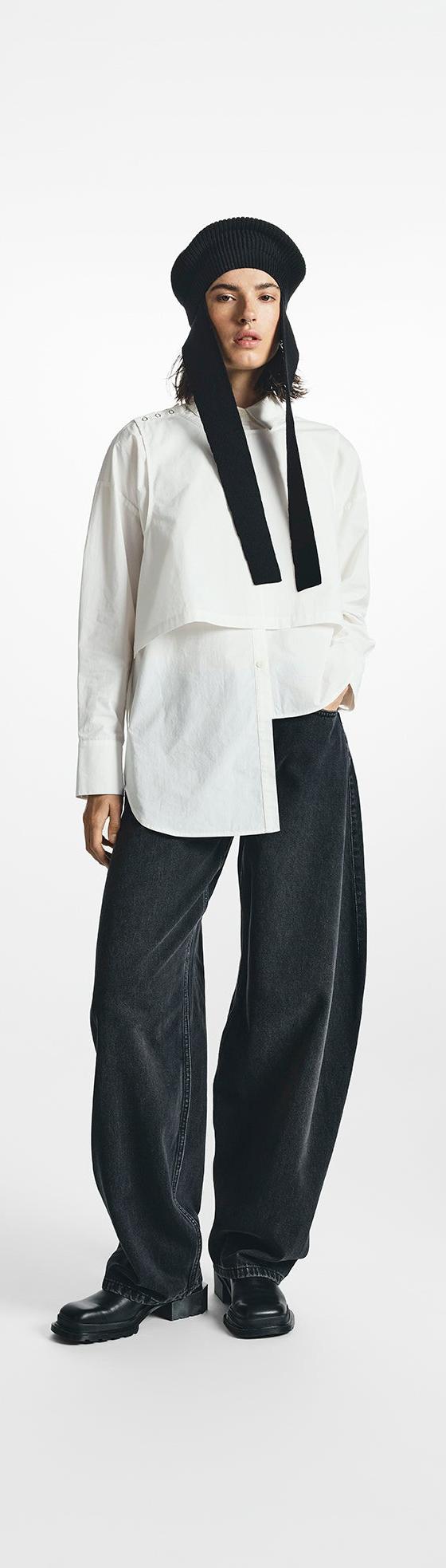 A woman wearing a white asymmetric STEL shirt with wide black denim trousers and a knit hood