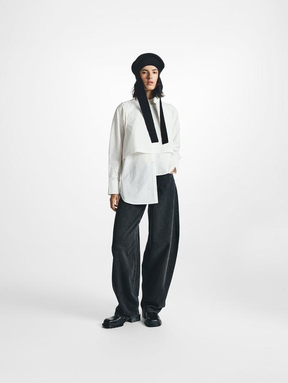 A woman wearing a white asymmetric STEL shirt with wide black denim trousers and a knit hood