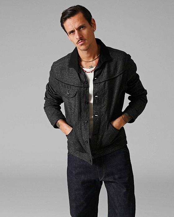 A man wearing a dark tweed Stevenson Overall Co. Western jacket with indigo selvedge denim jeans
