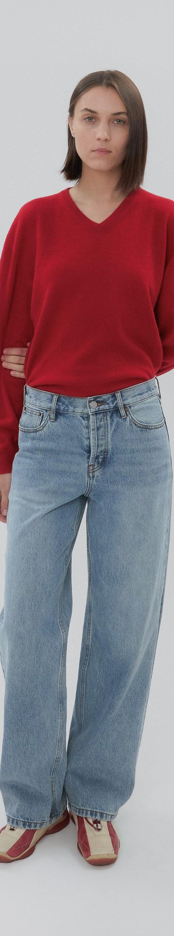 A woman wearing a red V-neck sweater with light-wash Still Here wide-leg jeans