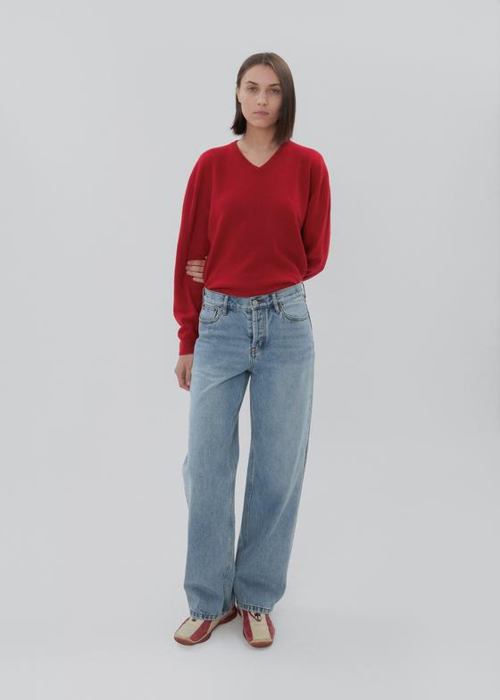 A woman wearing a red V-neck sweater with light-wash Still Here wide-leg jeans