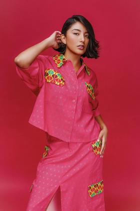 A woman wearing a pink patch-pocket camp shirt and matching midi skirt