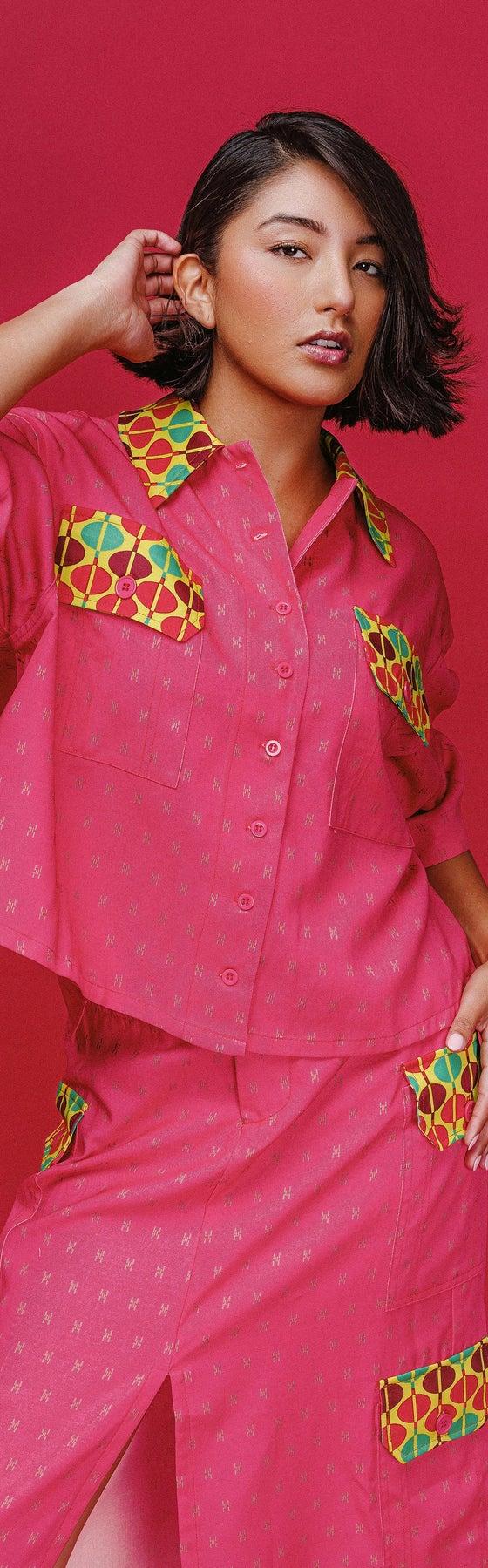 A woman wearing a pink patch-pocket camp shirt and matching midi skirt