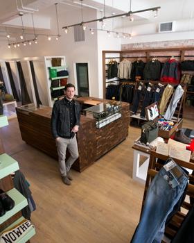 A man in a dark denim jacket standing in a menswear boutique lined with denim, knitwear and shirting