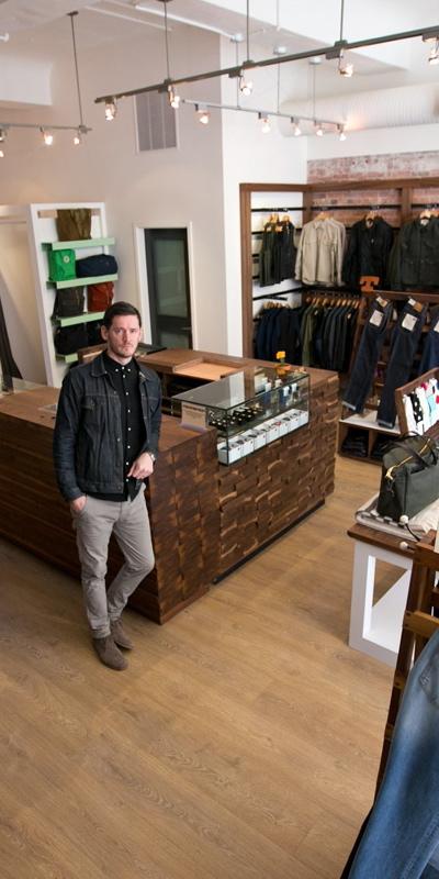 A man in a dark denim jacket standing in a menswear boutique lined with denim, knitwear and shirting