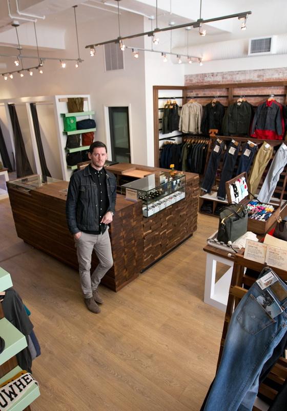 A man in a dark denim jacket standing in a menswear boutique lined with denim, knitwear and shirting