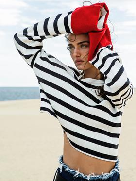A woman wearing a black and white striped Stradivarius sweater with frayed denim shorts on the beach