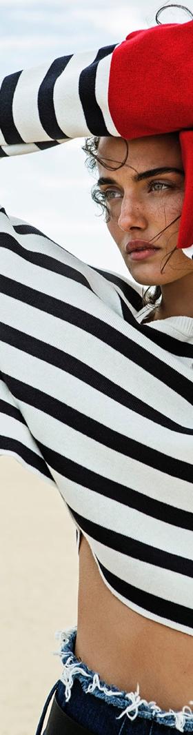 A woman wearing a black and white striped Stradivarius sweater with frayed denim shorts on the beach