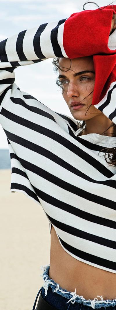 A woman wearing a black and white striped Stradivarius sweater with frayed denim shorts on the beach