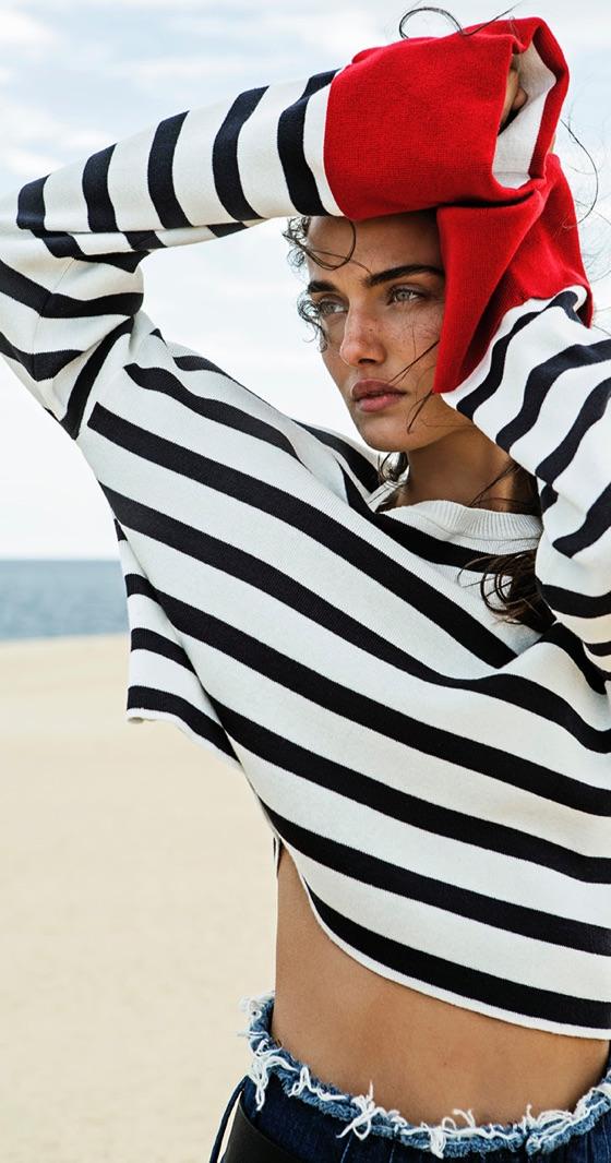 A woman wearing a black and white striped Stradivarius sweater with frayed denim shorts on the beach