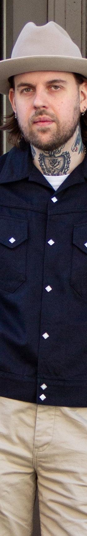 A man wearing a navy Sugar Cane jacket with khaki trousers and a felt hat