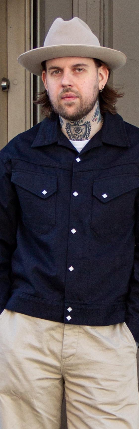 A man wearing a navy Sugar Cane jacket with khaki trousers and a felt hat