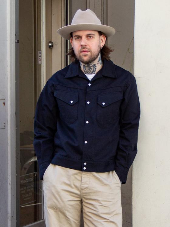 A man wearing a navy Sugar Cane jacket with khaki trousers and a felt hat