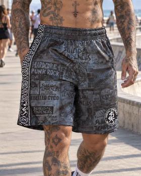 A tattooed man wearing grey Suicidal Tendencies x Sullen Clothing mesh shorts at a skatepark
