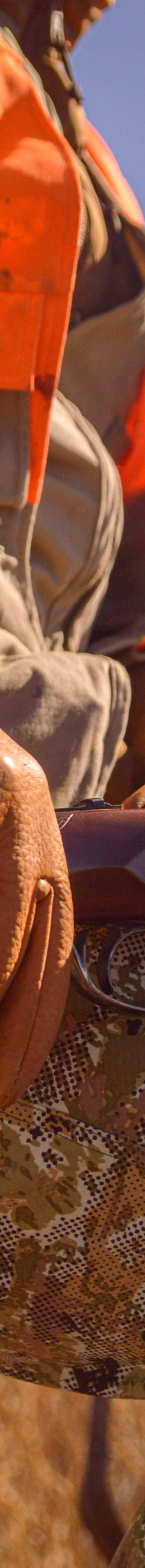 A hunter wearing tan Sullivan Glove Co leather gloves resting on a shotgun in an open field