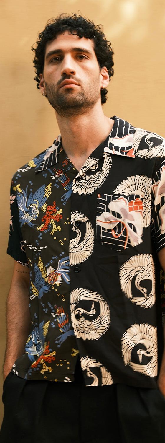 A man wearing a black Sun Surf rayon aloha shirt with Japanese crane and fan motifs