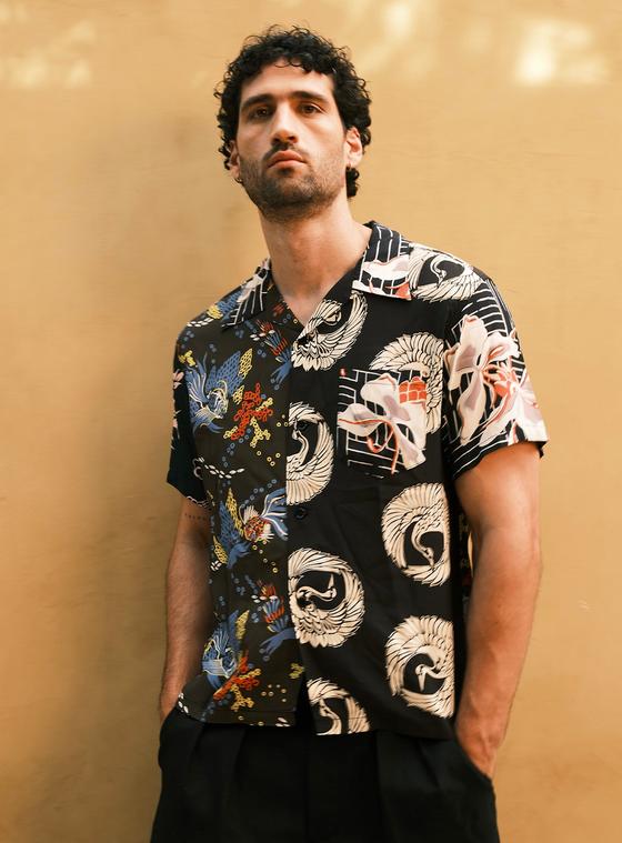 A man wearing a black Sun Surf rayon aloha shirt with Japanese crane and fan motifs