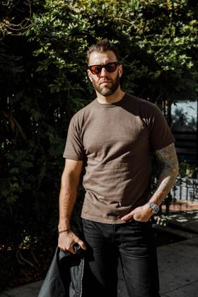 A man wearing a brown Sunray Sportswear t-shirt with black jeans