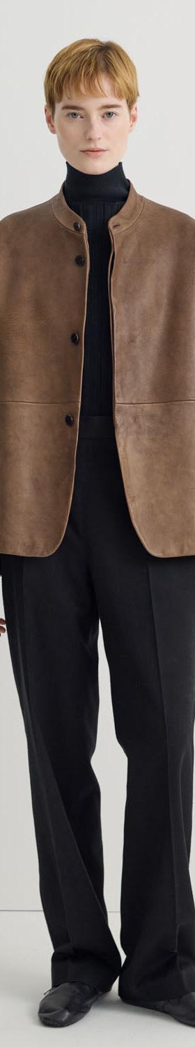 A woman wearing a brown suede Taiga Takahashi jacket with a black turtleneck and black trousers