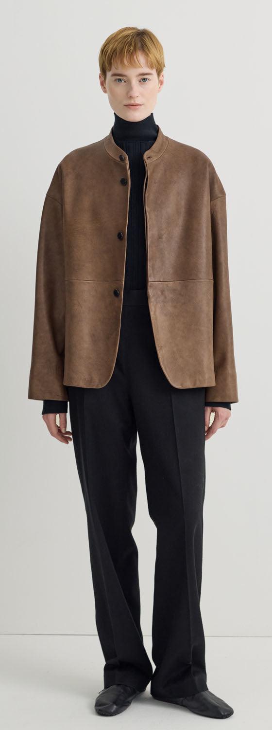 A woman wearing a brown suede Taiga Takahashi jacket with a black turtleneck and black trousers